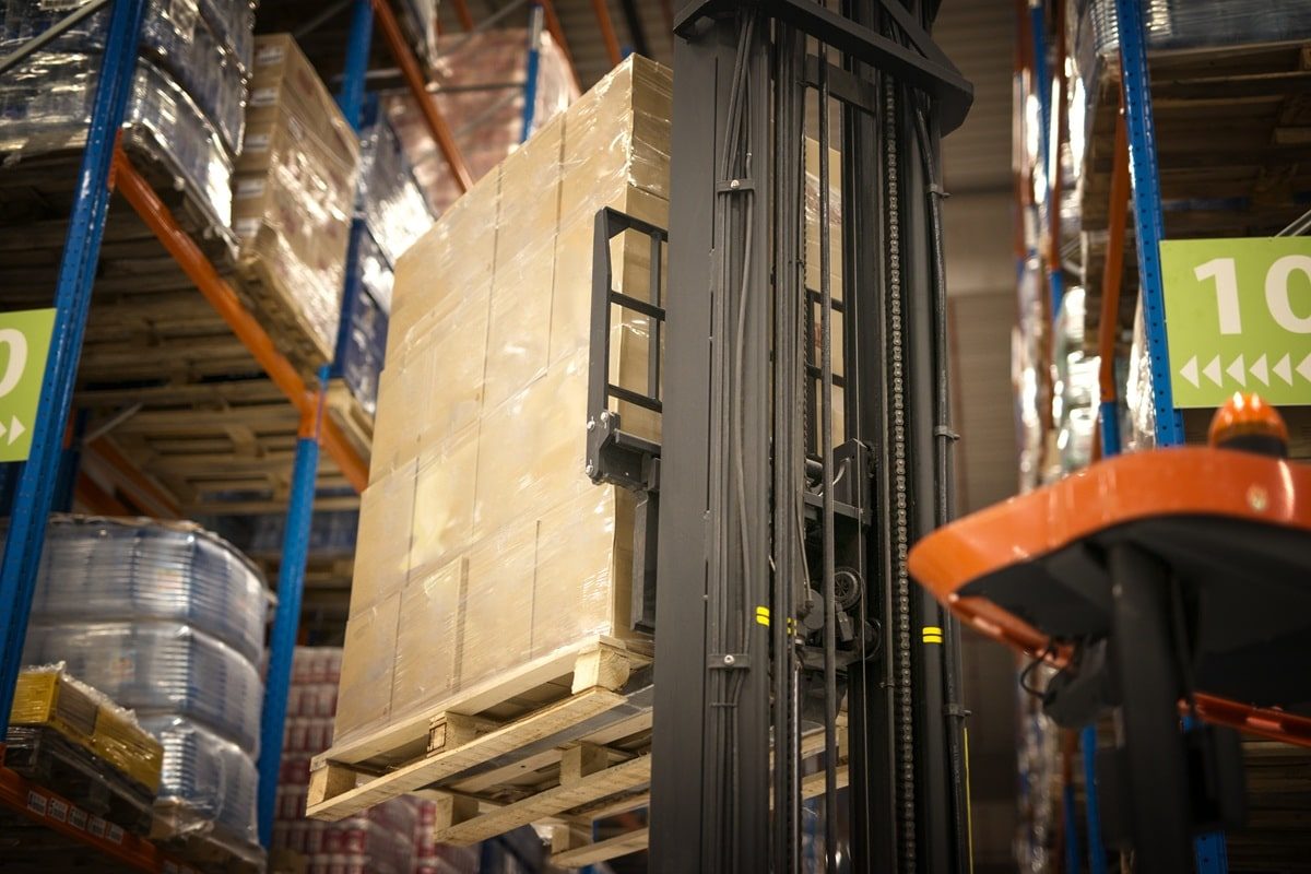 Empilhadeira movendo pilhas de caixas em um armazém, destacando a eficiência na logística e armazenamento de produtos em prateleiras no modelo de estoque vertical.